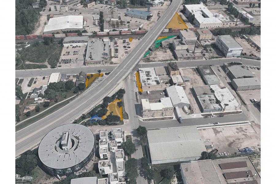 Aerial view of an industrial district with a raised highway, warehouses, a circular building, and yellow, green, and blue highlighted areas.