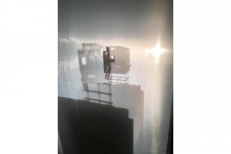 Hazy city skyline seen through a rain-speckled window, with rooftop structures silhouetted against bright sunlight, creating a quiet mood.
