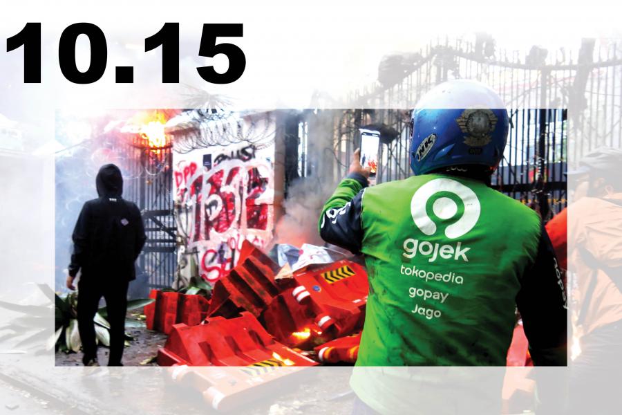 Composite protest image dated 10.15: a Gojek rider faces a smoky, barricaded street with burning debris and graffiti, conveying unrest and tension.