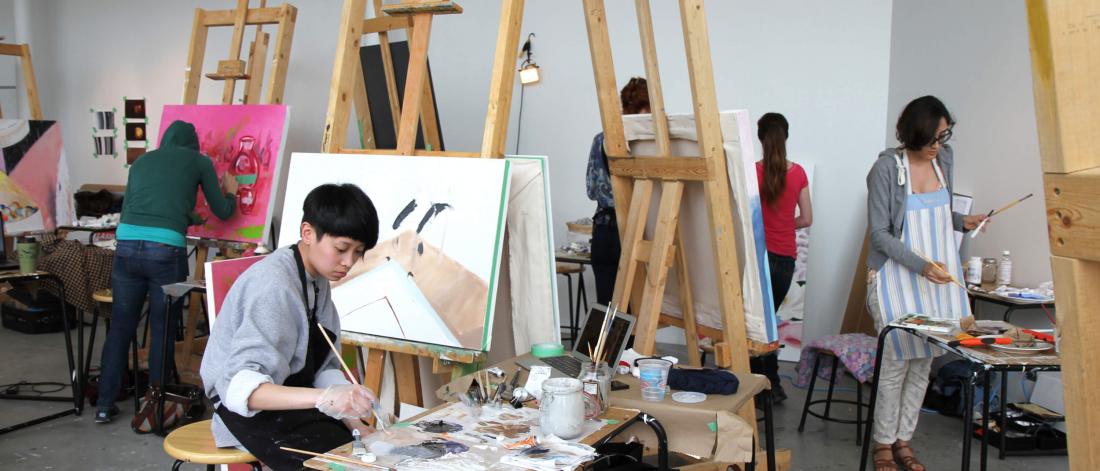 Students work on painting projects at easels in a painting studio. 