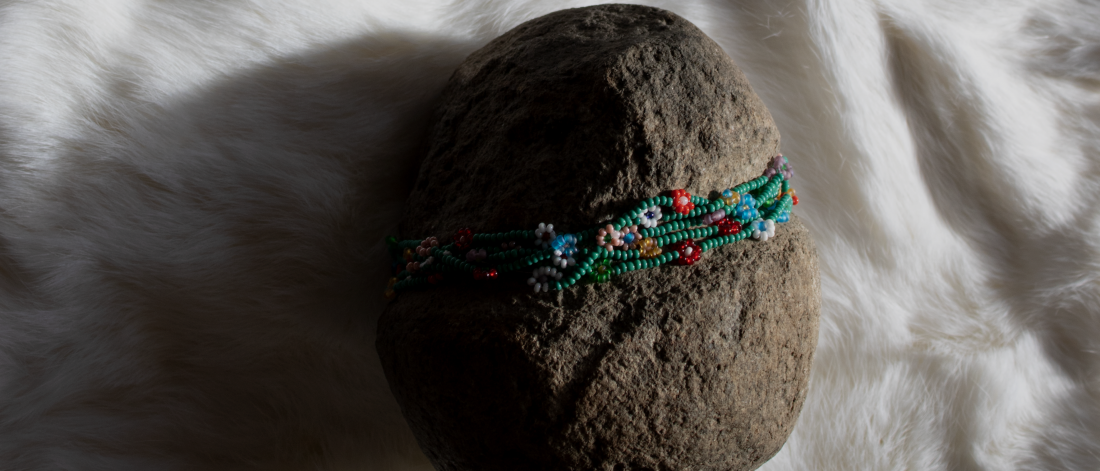Image of work by Audie Murray, entitled "chi fii embraces the old ones", Featuring a rock wrapped in a floral pattern beaded chain. Placed on a white fur throw.