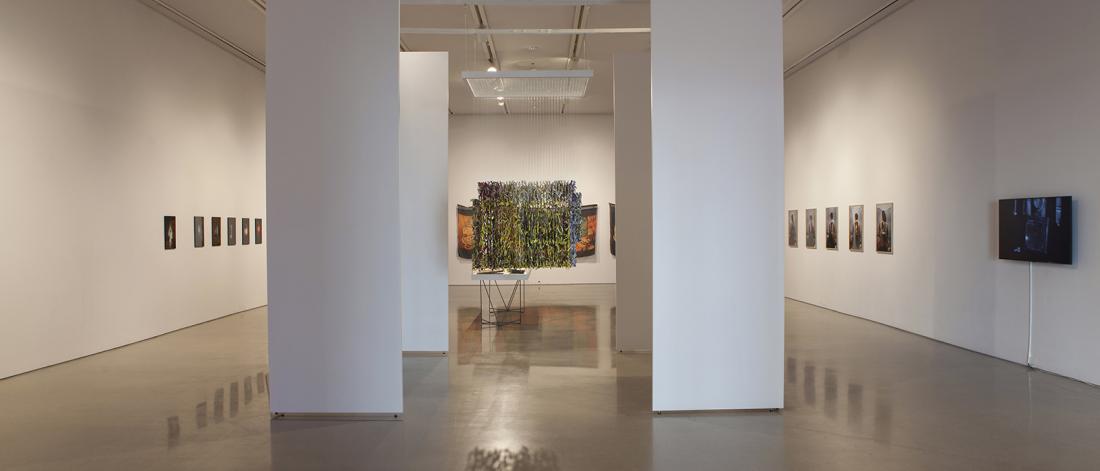Gallery installation view featuring large sculptural and photographic works, flanked by tall white pillars.