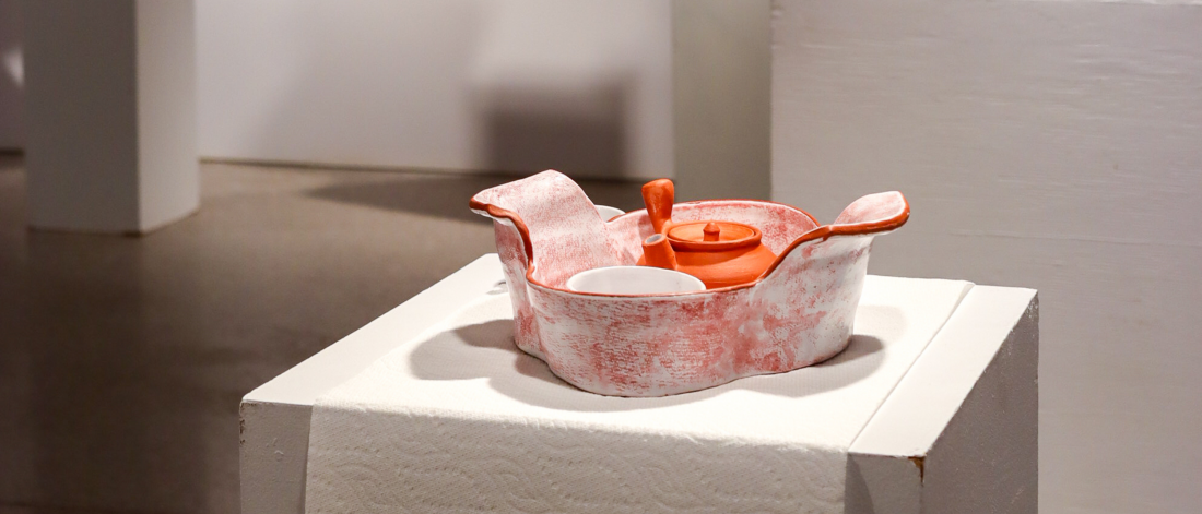 A red and white ceramic tea set displayed on a white pedestal in a gallery setting.