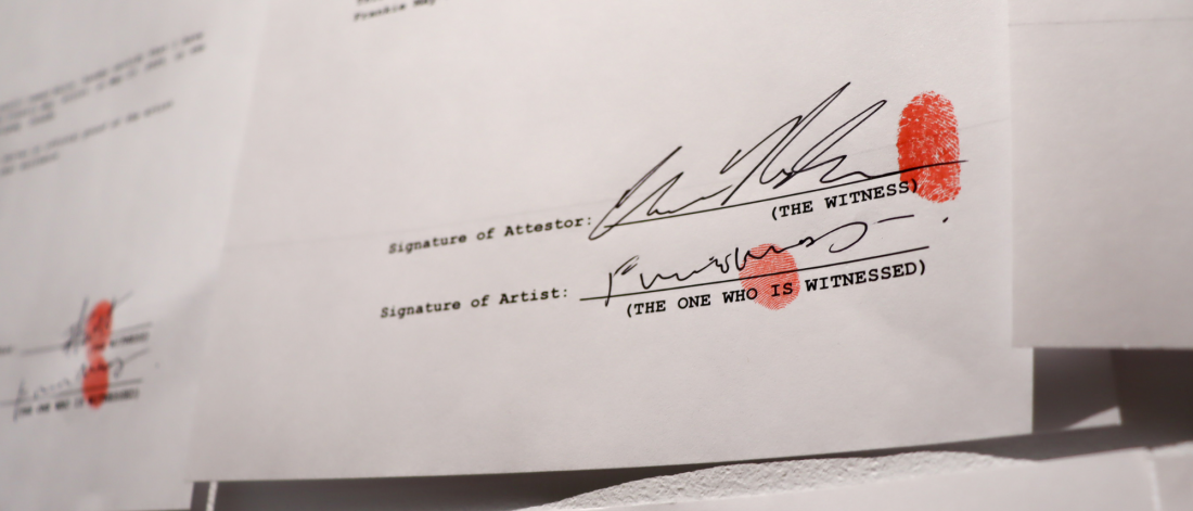 A close-up of a printed document showing signatures labeled “Signature of Attestor” and “Signature of Artist.” Both are signed with red thumbprints next to the text “(THE WITNESS)” and “(THE ONE WHO IS WITNESSED).”