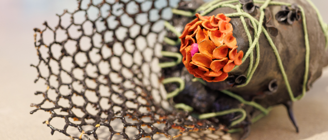 A sculptural work by Diana Sofia Lozano wrapped in green string features an orange flower-like form and a black lattice structure.