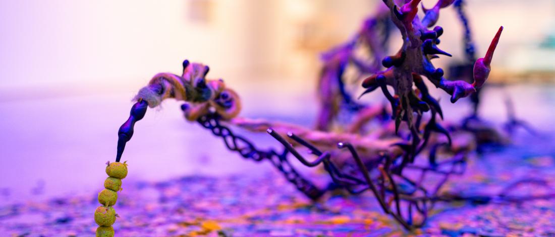 Twisted sculptural form with yellow beads and wool on a confetti-covered floor.