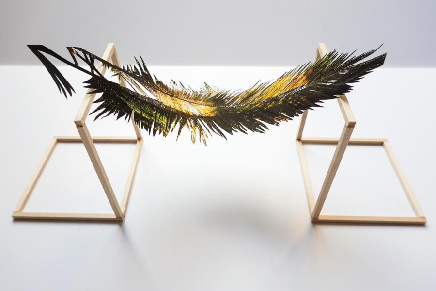 A metallic feather rests on a wooden stand. 