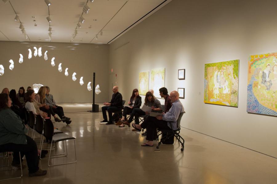 An inside look at the School of Art Gallery with some pieces on display while a crowd of seated guests sit in front of a panel of 5 people.