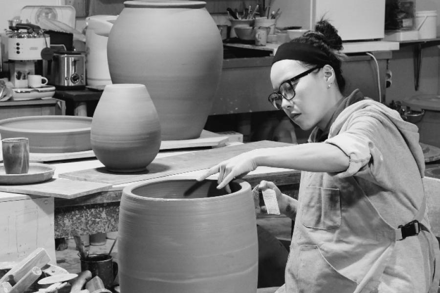 Grace Han sit behind a potters wheel, her hands moulding a large cylindrical shaped vase.