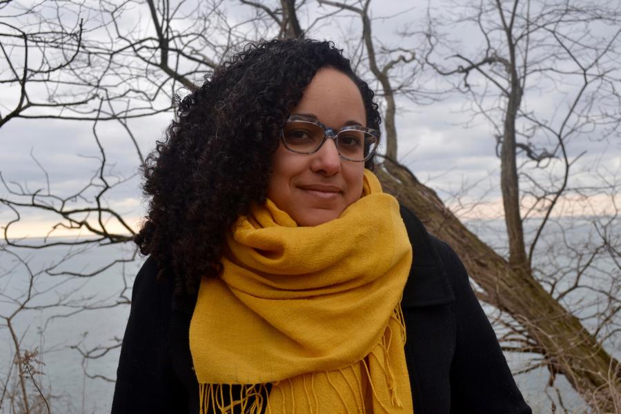 Erika De Freitas smail towards the camera wearing dark rammed glasses and a large yellow scarf