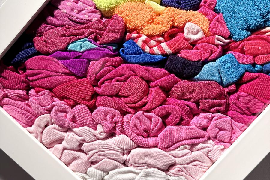 A colourful array of sock, stacked and squished together in a flat glass box, displayed on a wall