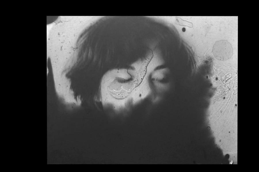 grainy still photo from a black and white film showing the face of a women with short dark hair, eyes closed, looking down. 