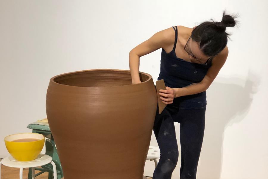 Grace Han stands working on a large clay clay vase on a pottery while