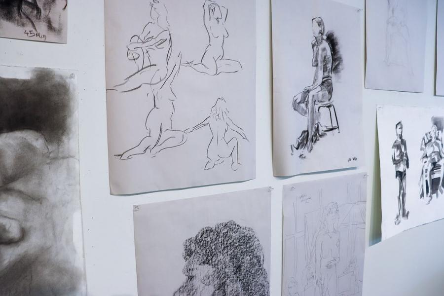 A collection of figure drawings pinned on a wall, showcasing various poses and sketch styles.
