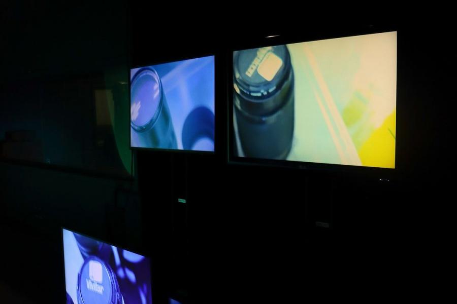 Screens display close-up images of lenses and photography equipment in a dimly lit room.