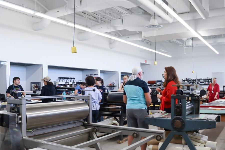 People interact in a printmaking studio filled with large presses and tools.