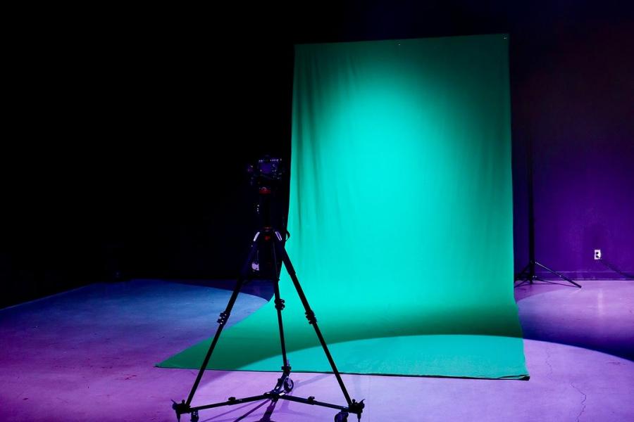A green screen setup with a camera on a tripod in a dark studio space.