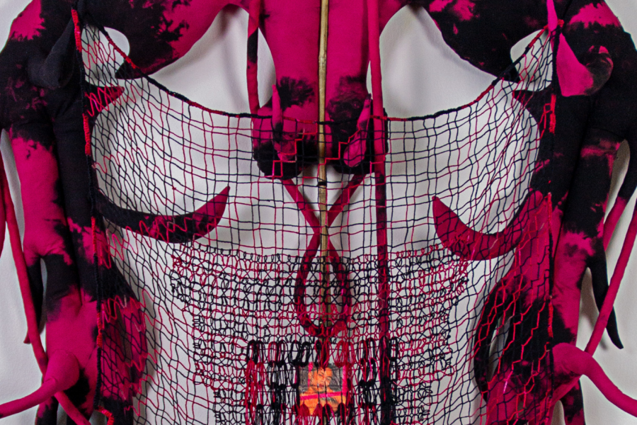 A sculptural textile piece with black and pink fabric, wire grid base, and glowing central element, resembling horns or tendrils extending outward.
