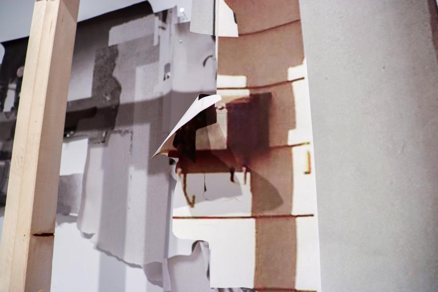 A detailed shot of a folded piece of collage paper revealing a printed photographic fragment underneath.