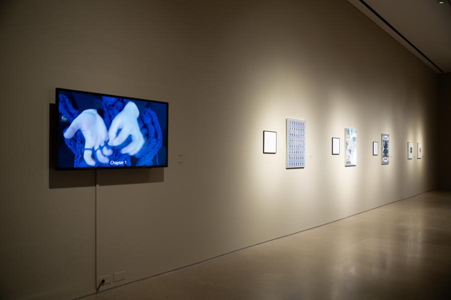 Video projection of weaving hands alongside framed multimedia artworks