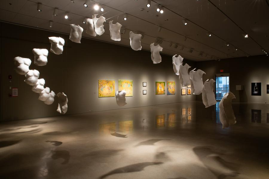 A dynamic perspective of the suspended torso installation, with the forms casting dramatic shadows on the floor and complementing the surrounding artwork in the gallery.