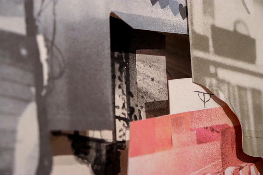 A detailed shot of a folded piece of collage paper revealing a printed photographic fragment underneath.