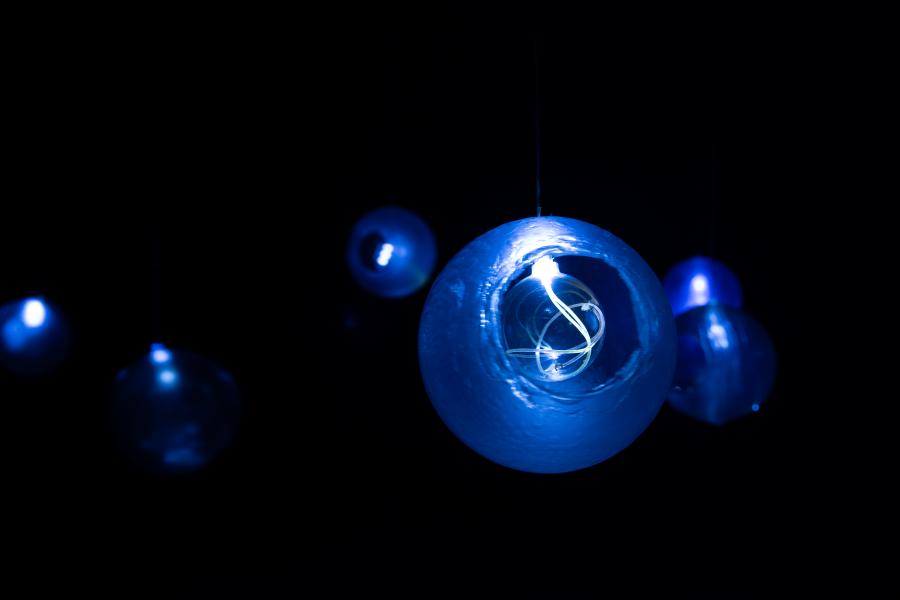 A suspended glowing blue glass orb with visible internal spiraling wires, set against a black background with other orbs in soft focus.