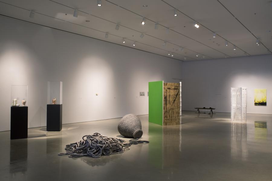 A gallery view with glass display cases, a coiled rope sculpture, a bright green panel, and wooden and white structural elements.