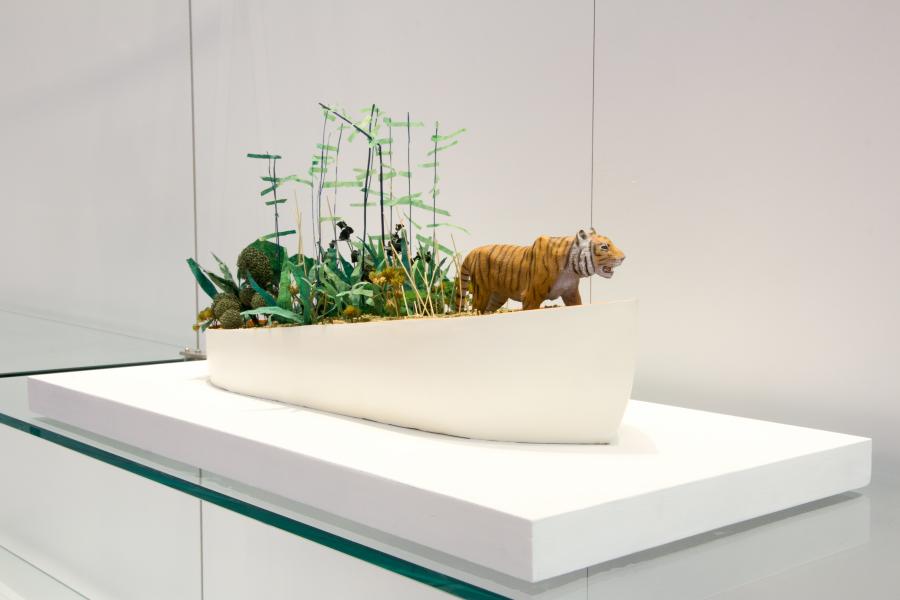 A model of a tiger in a boat surrounded by miniature plants and bamboo structures.