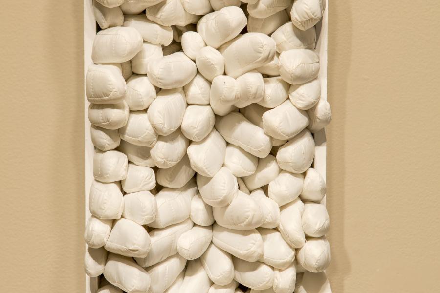 A detailed shot of a vertical wall installation composed of tightly packed, small white stones creating a textured column.