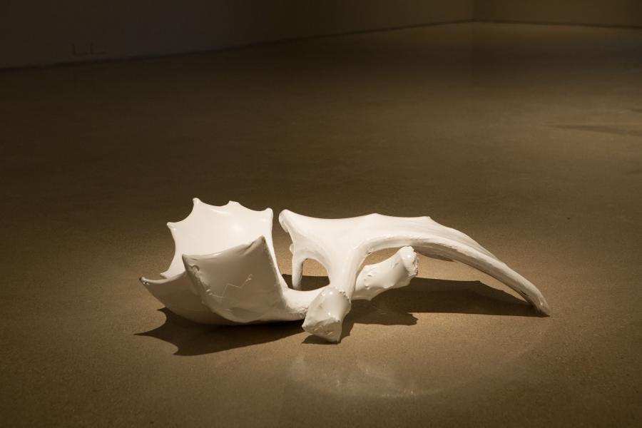 A close-up of a white ceramic sculpture on the gallery floor, resembling organic, bone-like shapes.