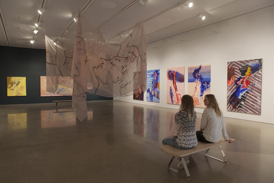 Two visitors seated in contemplation of Sheila Butler’s vibrant and evocative paintings, accompanied by a suspended translucent installation at the School of Art Gallery.
