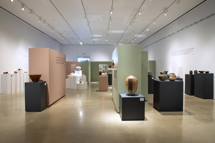 A wide-angle gallery shot featuring ceramics in cases and on pedestals with accompanying quotes on the walls.