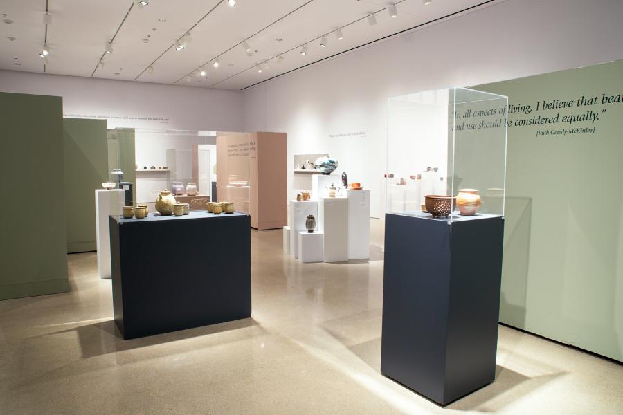 An array of ceramic vessels displayed in a well-lit gallery, complemented by thoughtful wall quotes and a clean aesthetic.
