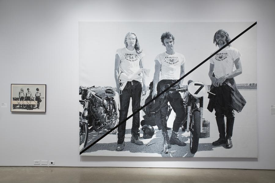 A striking black-and-white piece of large-scale artwork depicting motorcycle racers, accompanied by a smaller photo.