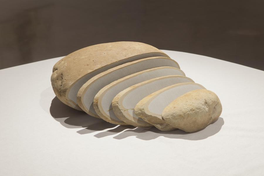 A close-up of a layered bread-like sculpture made of stone slices, placed on a white-clothed table.