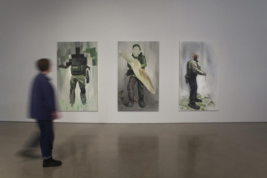 Three paintings depicting abstracted soldiers, viewed with a blurred visitor in the foreground.