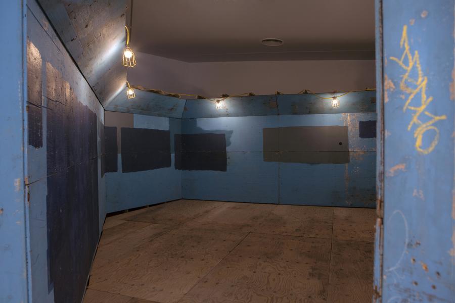 A view inside the blue wooden installation, showing textured and weathered surfaces under hanging lights.