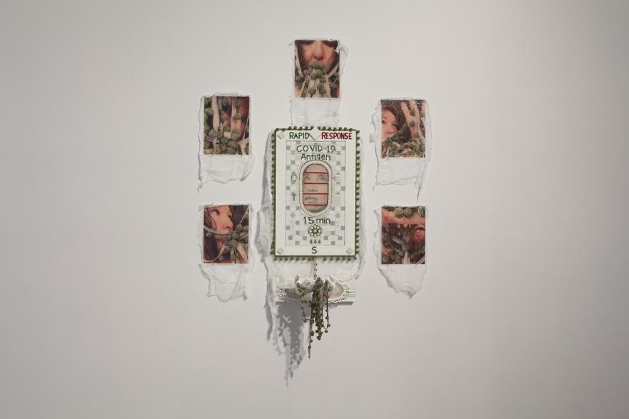 Mixed-media artwork incorporating a COVID-19 rapid test motif, embroidered details, and photographic fragments on fabric.