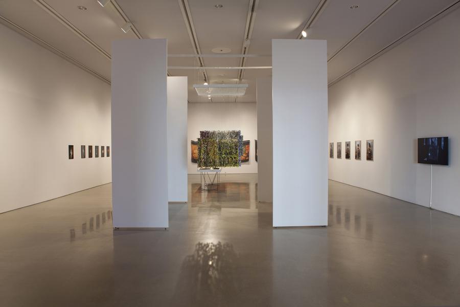 Gallery installation view featuring large sculptural and photographic works, flanked by tall white pillars.