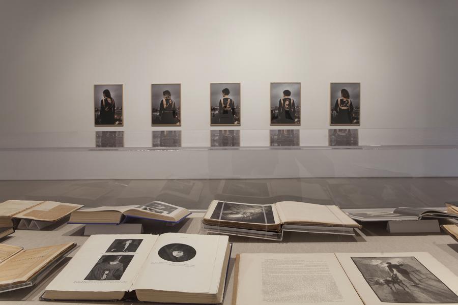 Archival books displayed under glass, with framed portraits of individuals in the background.