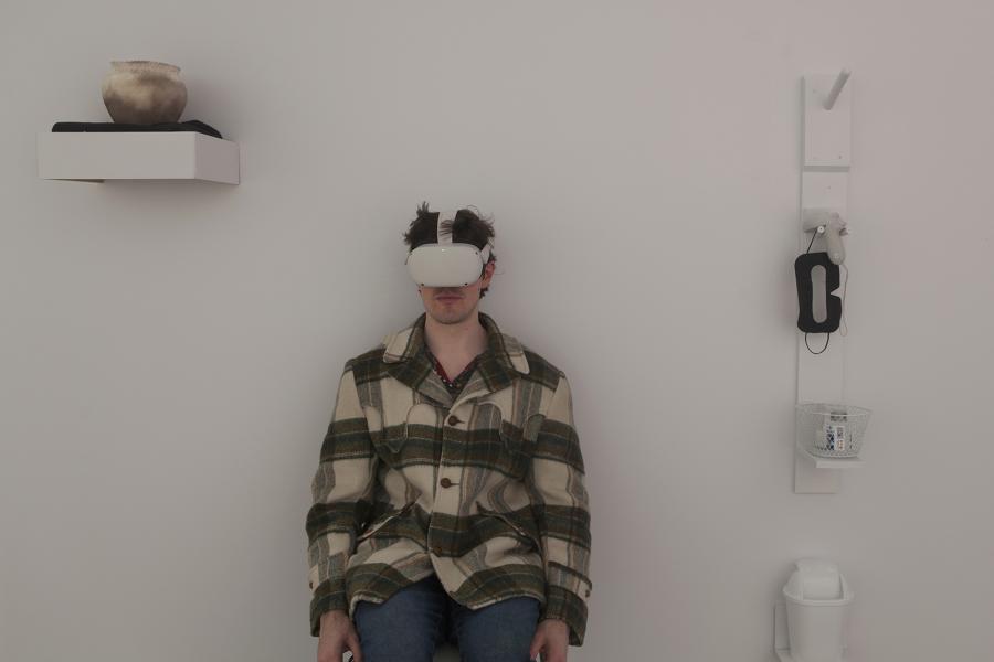 Seated figure wearing a VR headset in an installation space with interactive elements.