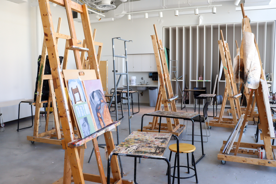 A bright, spacious painting studio filled with easels, tables, and in-progress artwork.