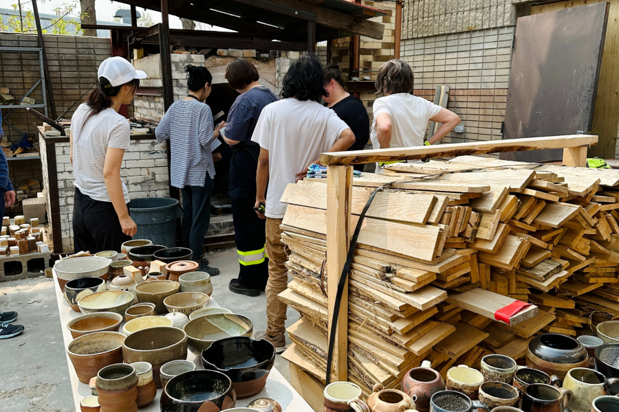 Students examine a wood-fired kiln with handmade ceramics laid out on tables nearby.
