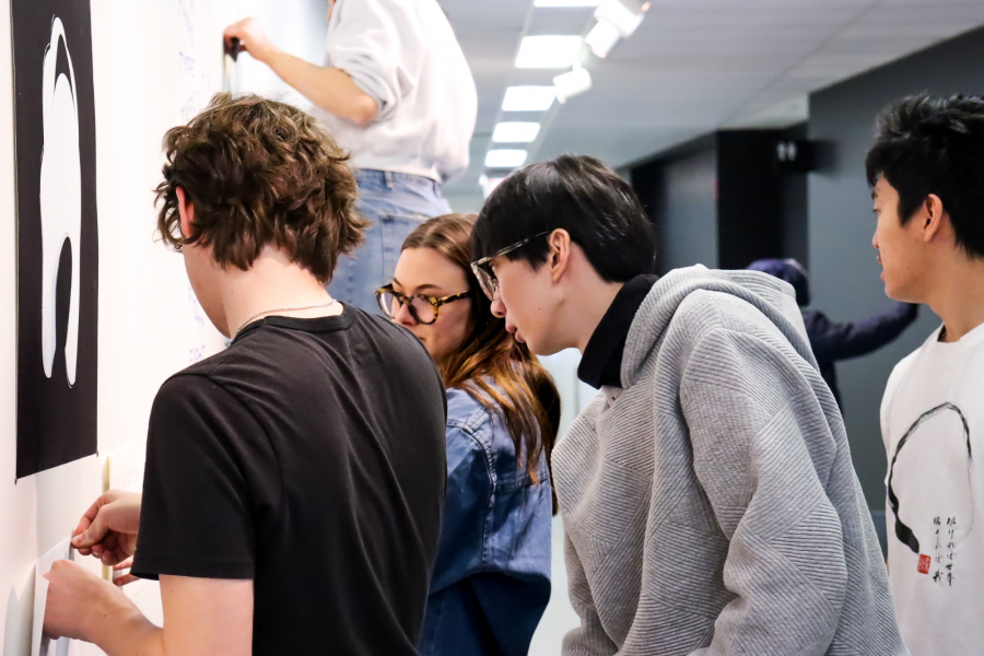 A group of students collaborate on installing graphic artwork on a hallway wall.