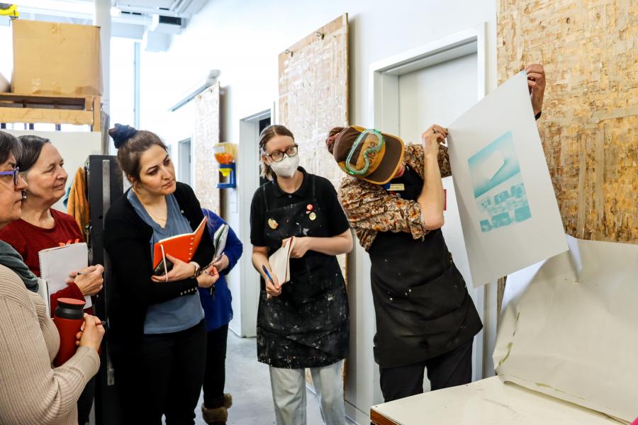 A visiting speaker presents a newly printed print to a class of students 