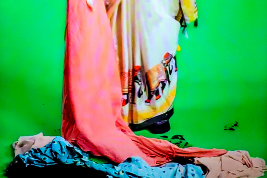 Close-up of fabric details from Laila Fazal’s performance video, showing a pink sari and elephant motif textile against a green screen floor, surrounded by scattered cloth.