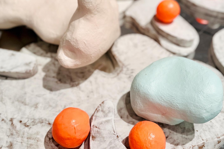 Detail of pastel sculptural forms and orange balls arranged on marbled bases.