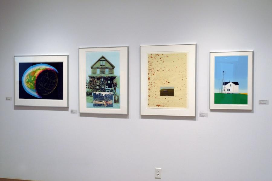 Four prints. From left to right: abstract green, yellow, and orange splashes in a blue-and-red bordered crescent, a blue-hued house and garden, red dots on a beige background with a small image of a brown homestead in the centre, and a white house with surrounding property in solid colours.