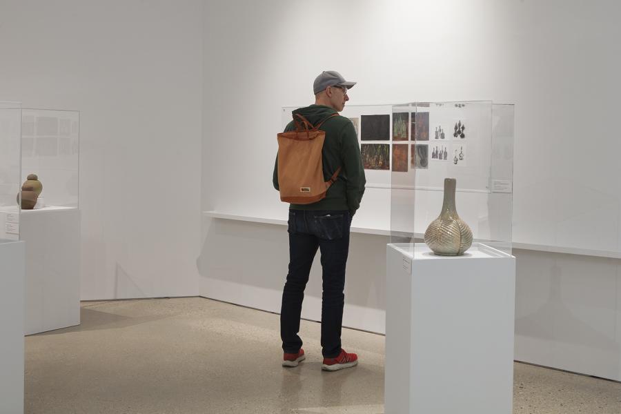 A visitor stands in the gallery viewing ceramic works and drawings from Robert Archambeau’s exhibition.